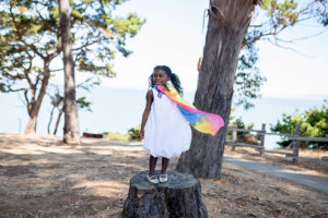 Girl wearing white dress and rainbow scarf on log