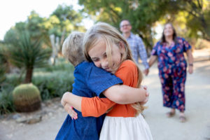 siblings giving a big hug with mom and dad in the background at stanford cactus garden