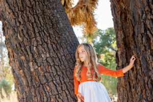 young girl standing at next to tree trunks, looking off in the distance