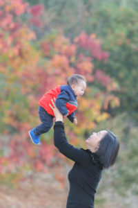 mom lifting up her boy with fall leaves in the background