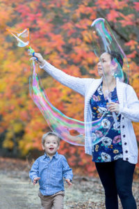 Mom playing with bubbles with son in front of fall leaves for fall family photos
