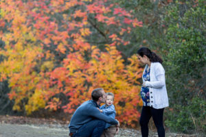 pregnant mom holding belly, dad kissing son in front of fall leaves for their fall family photos