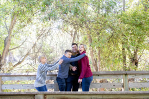 fall portraits at vasona park with family of four on a bridge with two boys running to parents