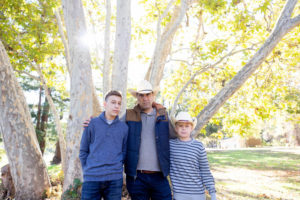 fall portraits at vasona park with dad in the middle of his two sons, he's wearing a cowboy hat
