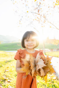 family photography san jose session with young girl wearing an orange dress and holding a bunch of fallen leaves