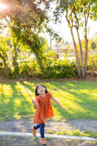 family photography san jose session of young girl wearing orange dress, holding sticks and laughing