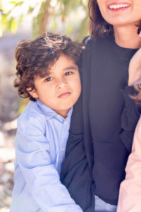 young boy looking at the camera with a crop of mom smile in the background