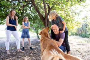 family of four laughing with the dog trying to lick a face