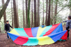 family of three in the redwoods playing with a giant parachute