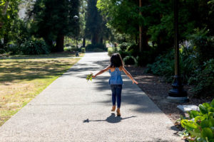 little girl holding leaves and walking down a path