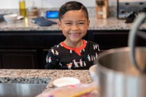 boy smiling in the kitchen wearing penguin pajamas while baking cookies