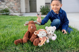three stuffed animals in the grass with the boy giving bunny ears to them