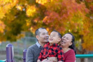 family of three laughing with fall colors in the background