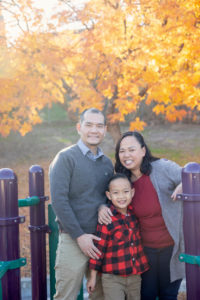family of three on a playground with yellow leaves behind them for their outdoor fall family photos