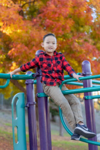 boy sitting on a playground with fall leaves behind him