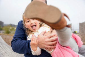 little girl being playful while sitting with her dad and kicking her leg up