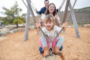 family of three playing on a wooden swing at presidio tunnel tops