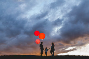 family of three with a pregnant mom and dad holding balloons for a silhouette photograph