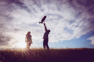 family of three with dad tossing kid in the air for silhouette photograph
