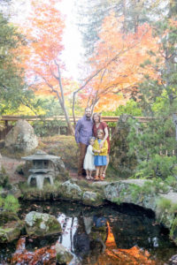 family of four portrait at the japanese gardens at the gardens lake Merritt in Oakland. the lake is reflecting their and there is a red maple behind them