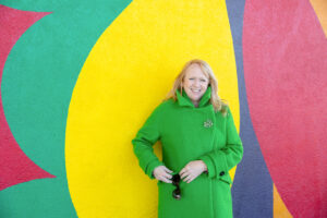 woman wearing a bright green jacket next to a colorful mural