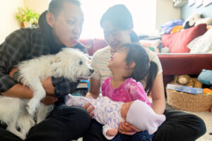 family of four sitting on the living room floor with the newborn baby and playing with the dog