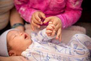 newborn baby girl holding her sister's fingers