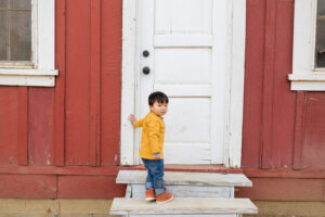little boy on the steps next to a red barn