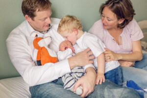 family of four newborn photo with dad holding baby, stuffed animal and toddler