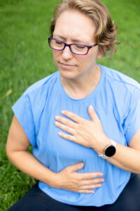 personal trainer sitting and holding her hands on her heart and stomach with her eyes closed