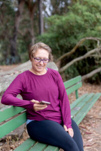 personal trainer sitting on a park bench with her phone in her hand
