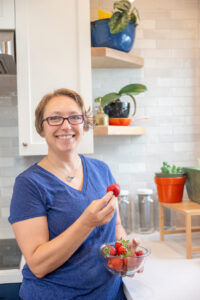 personal trainer and health coach standing in the kitchen holding a bowl of strawberries