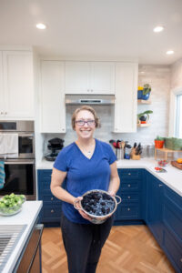 personal trainer and health coach standing in her kitchen holding a bowl of blueberries and berries