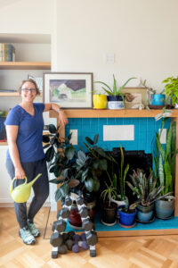 health and personal trainer standing next to plants and weights holding a watering can