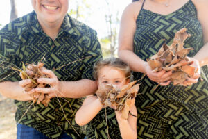 family of three holding pile of leaves