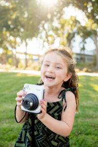 little girl holding an instax camera and smiling at the camera