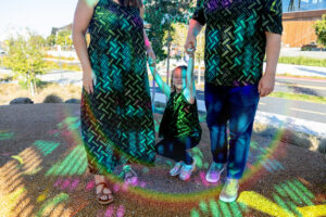 little girl holding parents hands with a lot of colors reflected onto them from google visitors center
