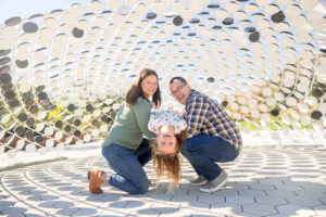 little girl upside down while parents hold her under art piece at google visitors center