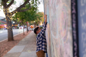 boy playing with chalk and writing on a mural in downtown los altos
