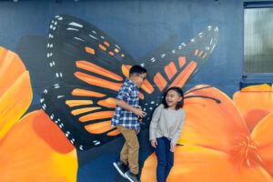 boy jumping and scaring his sister while she stands in front of a butterfly mural in downtown los altos