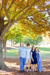 family of four wearing color blue under fall leaves for their family photos in san jose