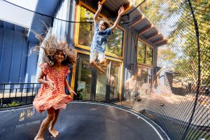 backyard family photos with two kids jumping on a trampoline